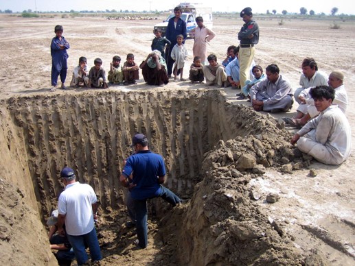 Researchers unwisely inspecting an unsupported excavation. On no account should anyone, ever do this, whether they are wearing hard hats or not.
